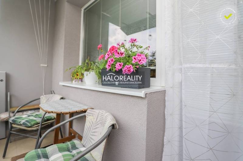 3 szobás lakás erkélye virágokkal és asztallal, ideális a pihenésre.