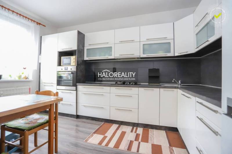 Konyha egy háromszobás lakásban fehér szekrényekkel és fa mintázatú padlóval.