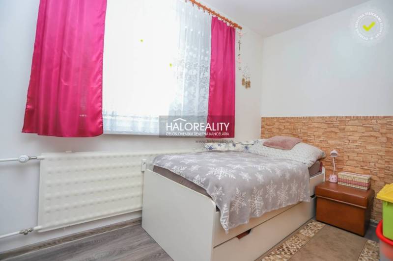 Szoba egy háromszobás lakásban ággyal, virágos függönnyel és fa dekorációjú padlóval.