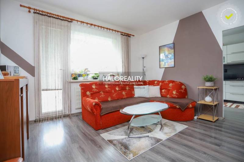 Nappali egy háromszobás lakásban narancssárga kanapéval és fa mintázatú padlóval.