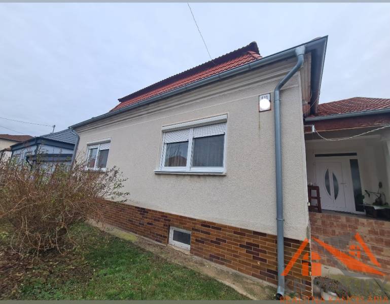 Családi ház Hurbanovóban világos homlokzattal és piros tetővel, bokrokkal körülvéve.