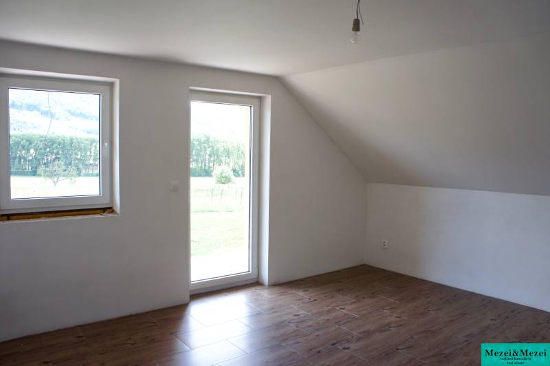 Világos szoba ablakokkal, fa dekoros padlóval és üvegajtókkal a családi házban.