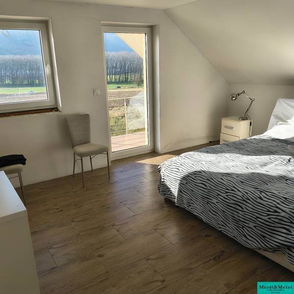 Világos hálószoba családi házban, ággyal, székkel és fa dekorációjú padlóval.