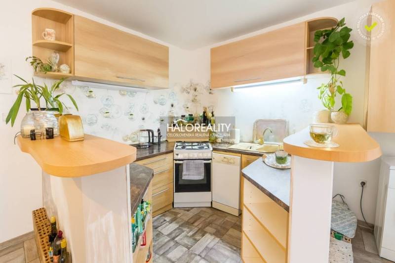 Konyha egy családi házban sarok konyhabútorral és fa dekorációval, dekoratív növényekkel a polcokon.