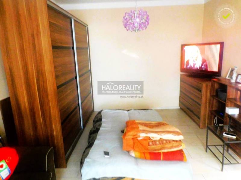 Hálószoba egy kétszobás lakásban ággyal, kanapéval és fa dekoros szekrénnyel.