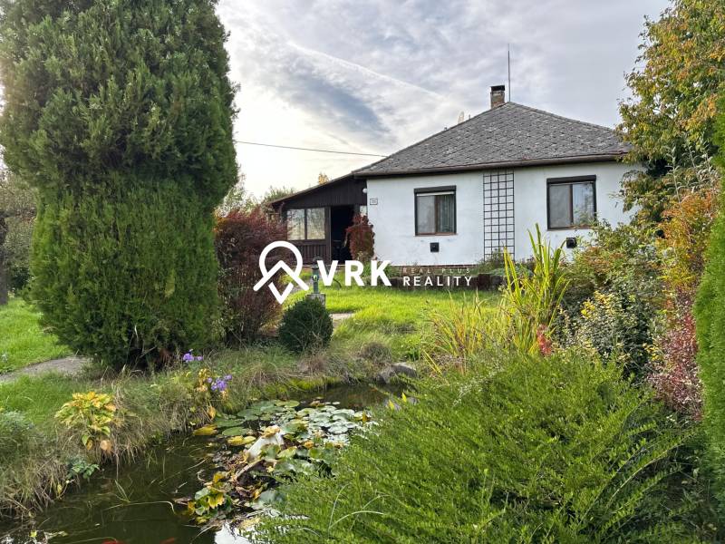 Családi ház Kalsa-ban gyönyörű kerttel és kis tóval, amelyet zöld növényzet vesz körül.