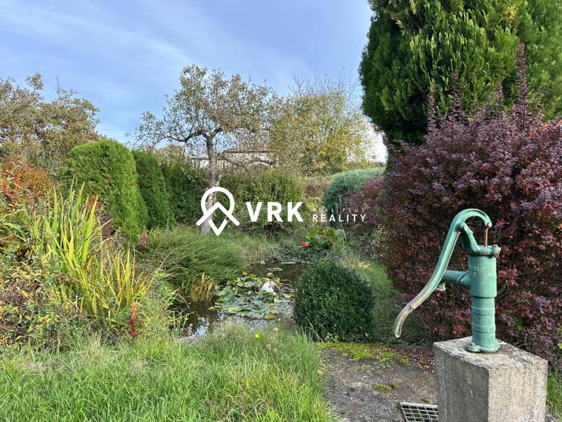 Egy családi ház kertje Kalšán régi szivattyúval és sok zölddel.