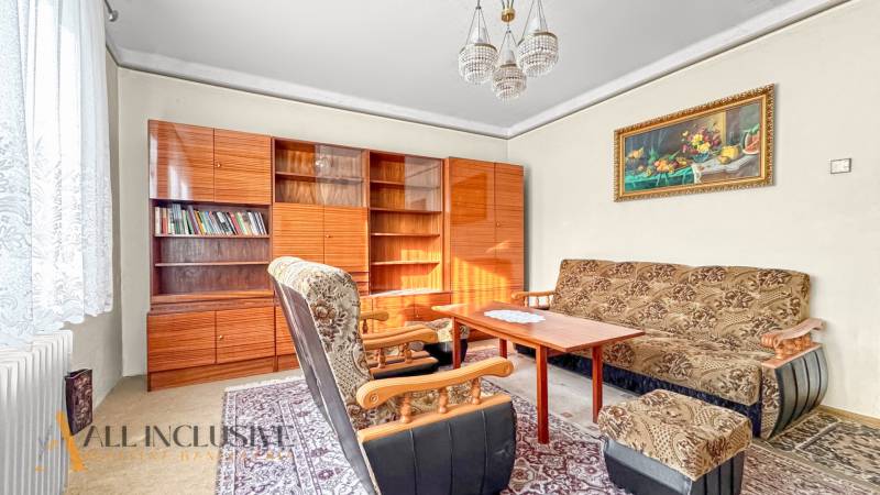 Nappali egy családi házban fotelekkel, szőnyeggel, könyvespolccal és függönyökkel.