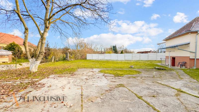 Udvar a családi ház mellett a Nemečkovská utcában, Prašiceben, kövezett területtel és fákkal.