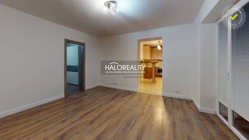 Nappali egy kétszobás lakásban, fa mintázatú padlóval és bejárattal a konyhába.