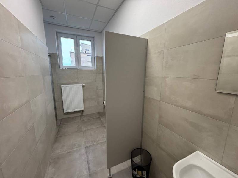 Irodák szürke burkolattal és WC-vel, kis ablakkal és bordás radiátorral.