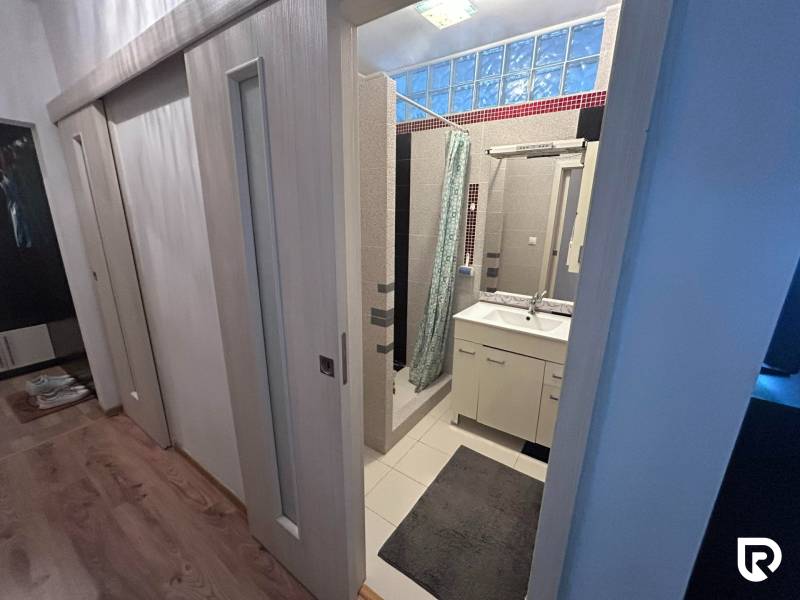 Fürdőszoba egy egyszobás lakásban mosdóval, zuhanyzóval és fa dekoros padlóval.