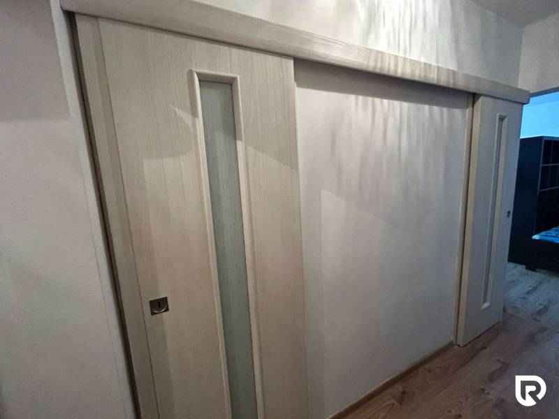 Tolóajtók üvegezéssel, fa mintázatú padló, 1 szobás lakás belső tere.