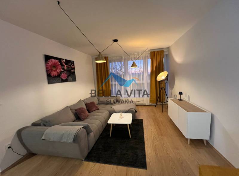 Nappali egy kétszobás lakásban kanapéval és fa mintázatú padlóval.