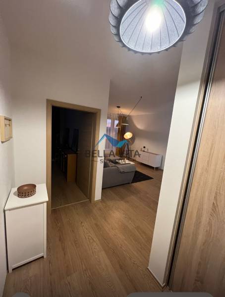 Folyosó egy kétszobás lakásban, fa mintázatú padlóval, amely a nappaliba vezet.