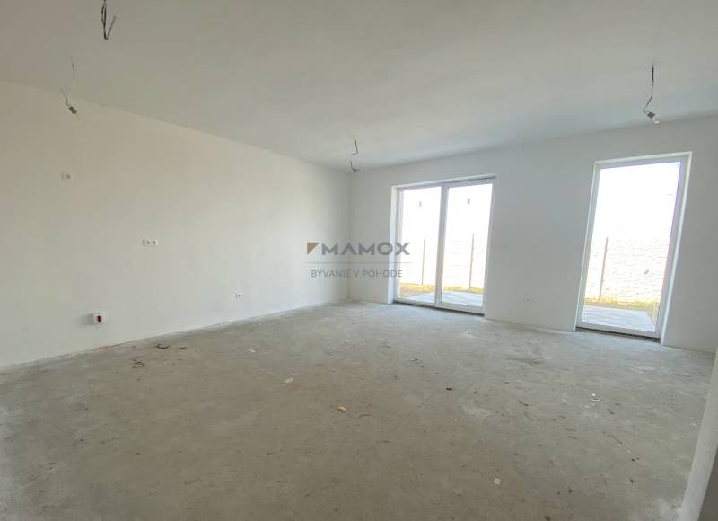 Tágas szoba egy családi házban betonpadlóval és nagy ablakokkal.