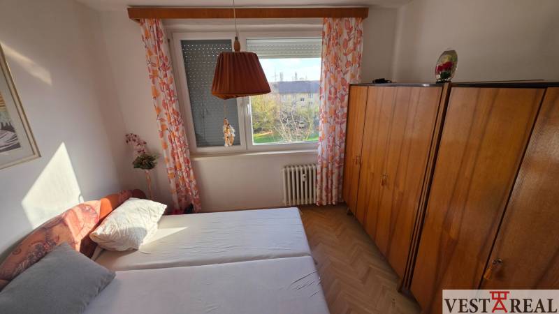 Hálószoba ággyal, szekrénnyel és fa dekorációjú padlóval egy háromszobás lakásban.