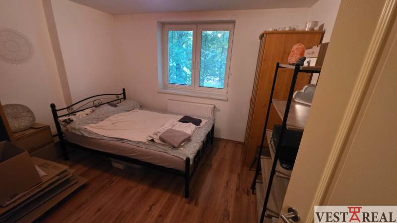 Hálószoba egy háromszobás lakásban fém ággyal és fa dekoros padlóval.