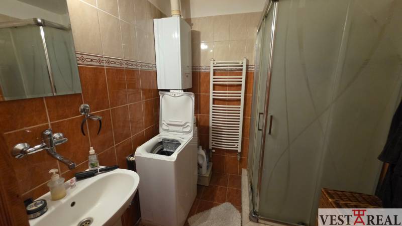 Fürdőszoba egy háromszobás lakásban mosógéppel, zuhanyzóval és kerámia burkolattal.