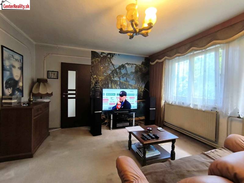 Nappali televízióval, kanapéval, asztallal és nagy ablakkal, családi ház.