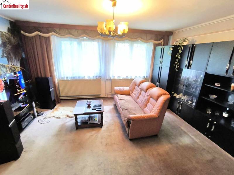 Nappali egy családi házban barna kanapéval, szekrényekkel és a falon lévő televízióval.