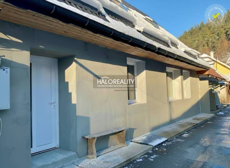 Családi ház Hroncban, hóval a tetőn, fehér ajtókkal és fa paddal.