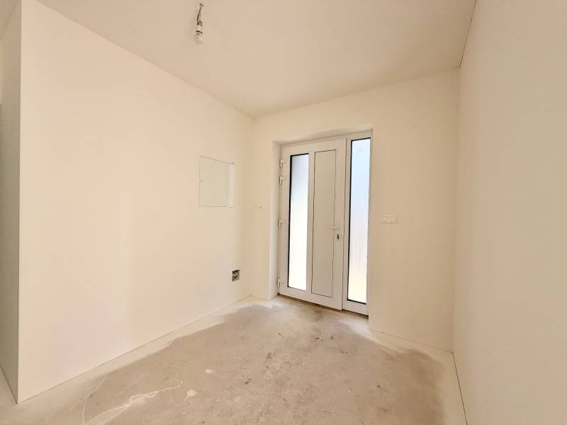 Üres szoba franciaajtókkal egy családi házban, fehér falak, betonpadló.