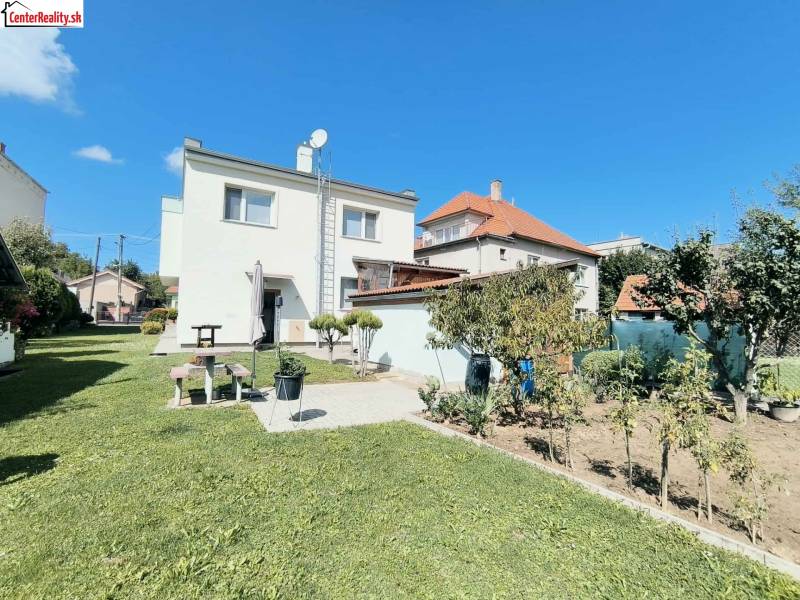 Családi ház Partizánskén, zöld gyep és kert veszi körül, kék ég alatt.