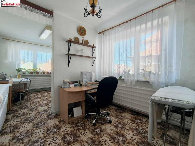 Szoba egy családi házban íróasztallal, növényekkel és virágmintás szőnyeggel.