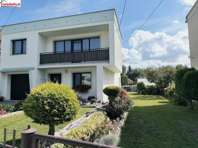 Családi ház Partizánskén, kerttel körülvéve, fákkal és zöld gyepes területtel.