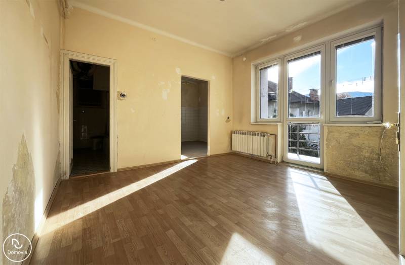 Egy 5 vagy több szobás lakás szobája, amelyet napfény világít meg és fa mintázatú padlóval rendelkezik.