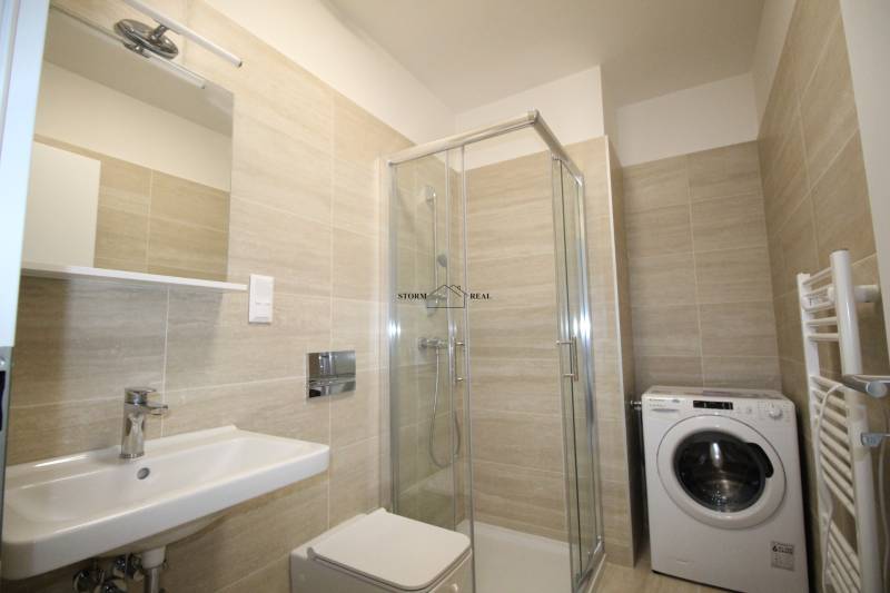 Fürdőszoba a garzonlakásban mosdóval, zuhanyzóval és mosógéppel.