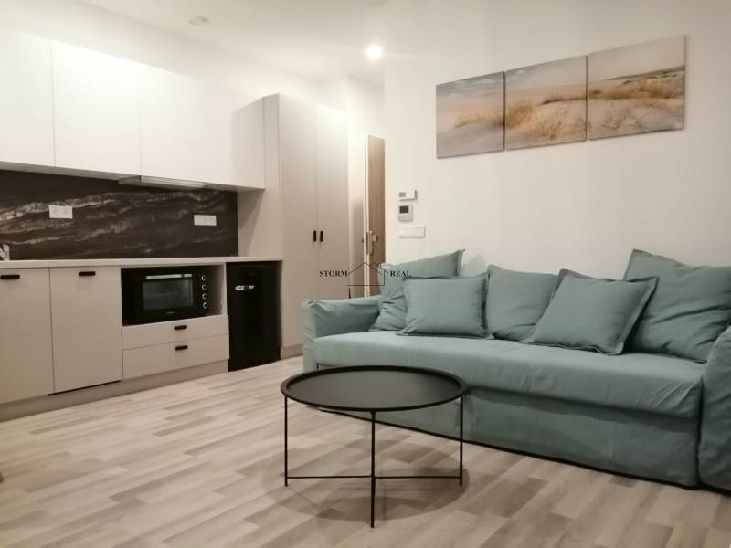 Garzonlakás konyhával, kék kanapéval, kerek asztallal és fa dekorációjú padlóval.