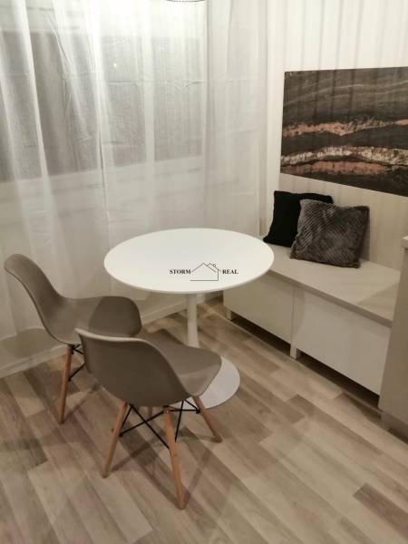 Étkező sarok kerek asztallal, két székkel és díszpárnákkal, fa dekorációjú padlóval.