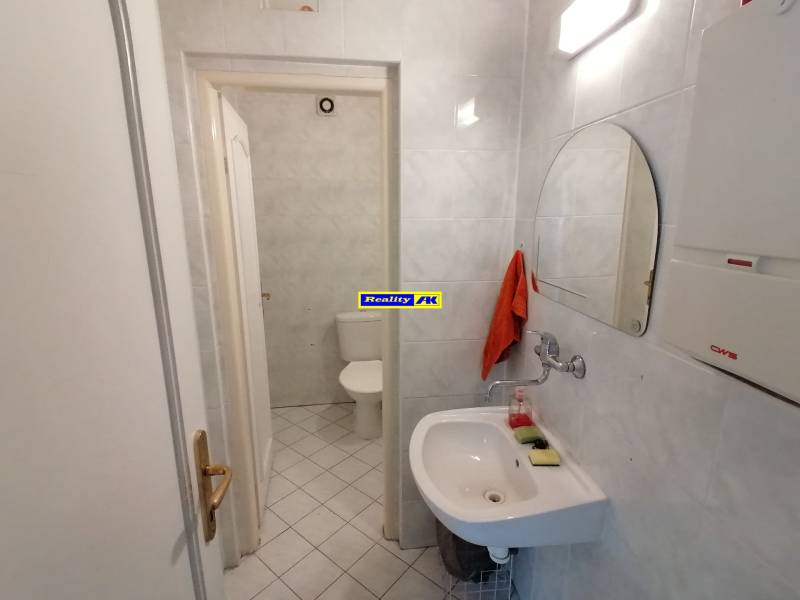 Iroda fürdőszobája tükörrel, mosdóval és WC-vel fehér csempéken.