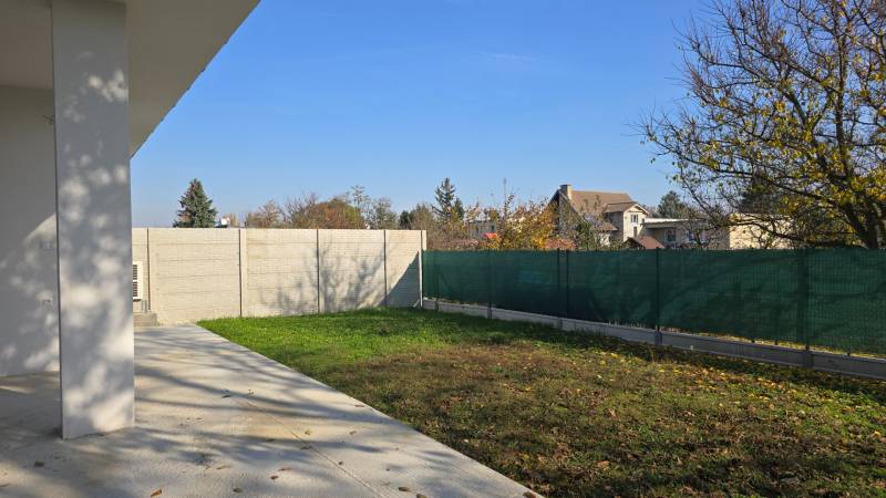 Családi ház kertje Pöstyénben gyepfelülettel, beton terasszal és kerítéssel.