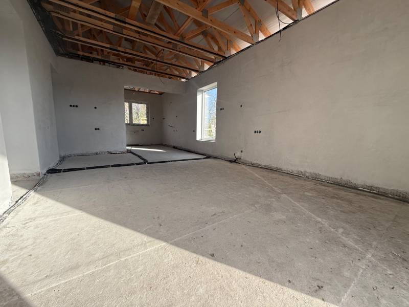 Családi ház belső tere betonpadlóval, fa gerendákkal és elektromos vezetékekkel.