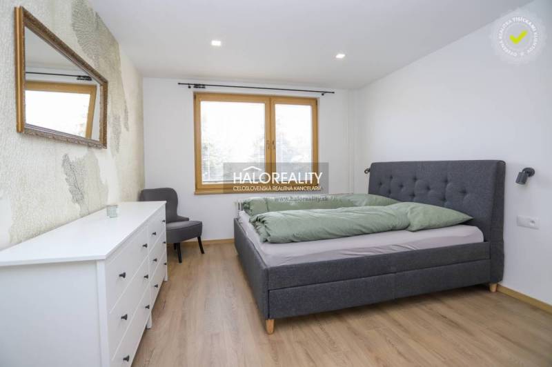 Hálószoba egy kétszobás lakásban ággyal, komóddal, tükörrel és fa mintázatú padlóval.