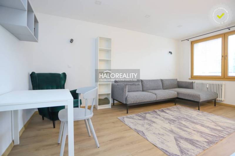 Nappali egy kétszobás lakásban kanapéval, asztallal, fotellel és fa dekorációjú padlóval.