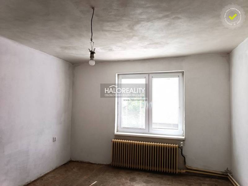 Üres szoba egy családi házban fehér falakkal, radiátorral és ablakkal.