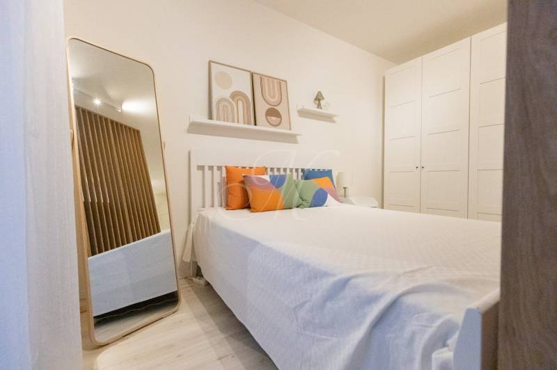 Hálószoba egy egyszobás lakásban ággyal, színes párnákkal, tükörrel és nagy szekrénnyel.