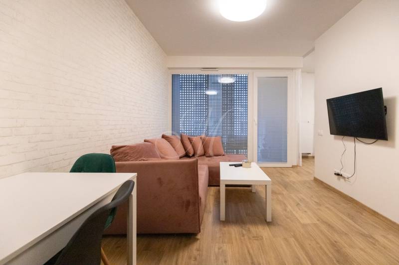 Nappali egy kétszobás lakásban kanapéval, televízióval és fa dekorációjú padlóval.