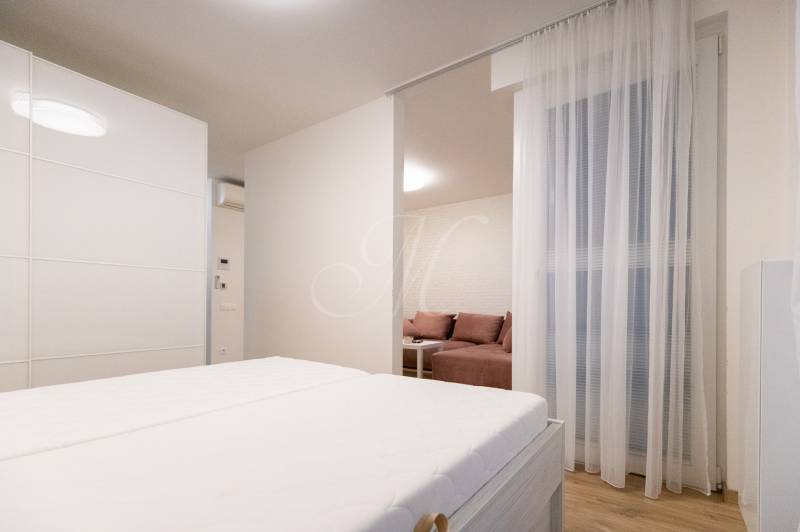 Kétszobás lakás ággyal, fa mintázatú padlóval és osztott nappali résszel.