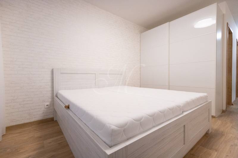 Világos hálószoba fehér ággyal, beépített szekrénnyel, fa dekorációjú padlóval egy kétszobás lakásban.