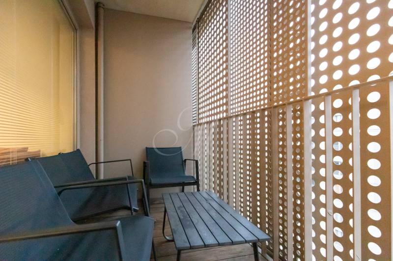 Erkély fa dekorációval, ülőgarnitúrával és perforált fallal egy kétszobás lakásban.