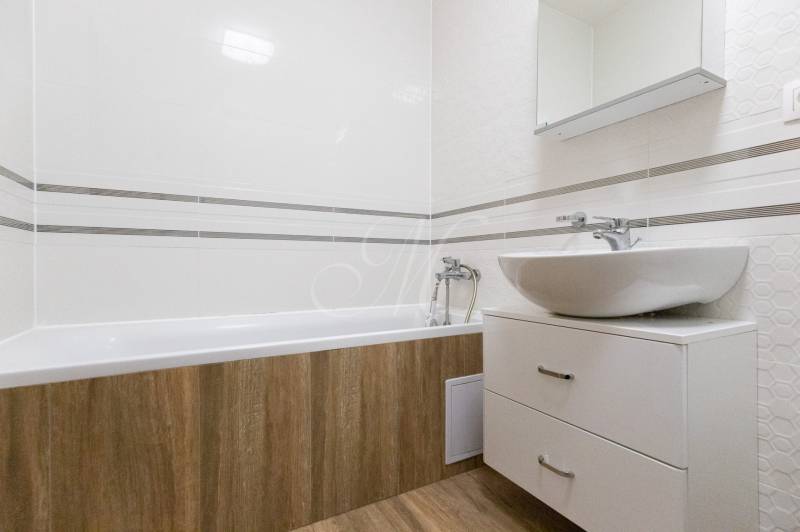 Fürdőszoba egy kétszobás lakásban káddal, mosdóval és fa dekoros padlóval.