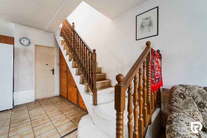 Családi ház belső tere lépcsőházzal, élénkvörös szőnyeggel és egy festménnyel a falon.