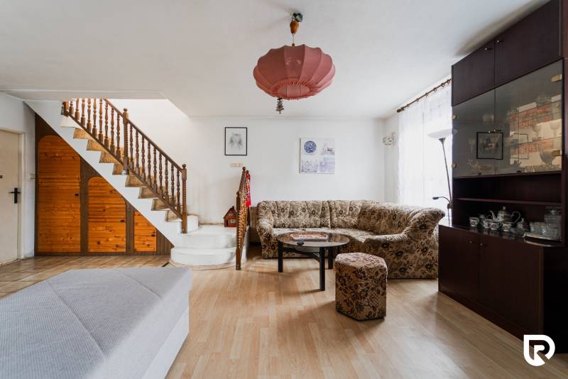 Nappali családi házban fa lépcsővel, kanapéval, szekrénnyel és fa mintázatú padlóval.