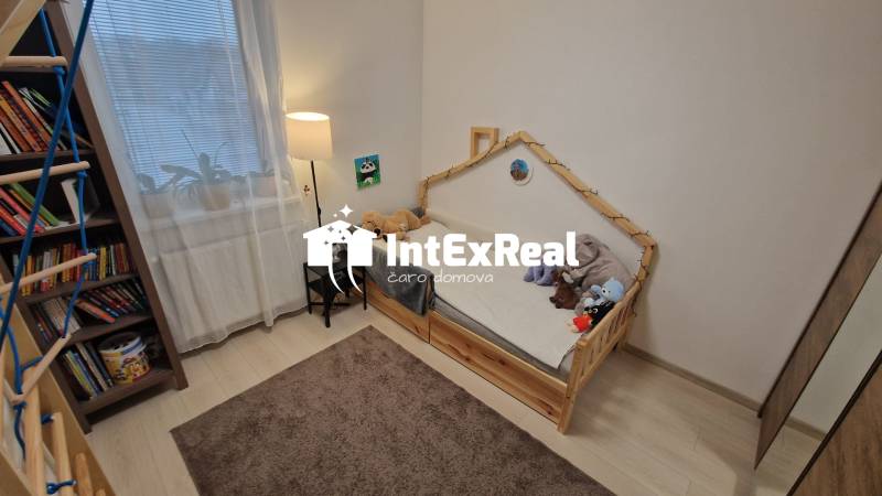 Gyerekszoba egy háromszobás lakásban, világos padlóval és könyvekkel teli polccal.