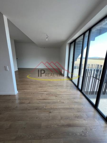 Világos nappali egy kétszobás lakásban, fa hatású padlóval és nagy ablakokkal.